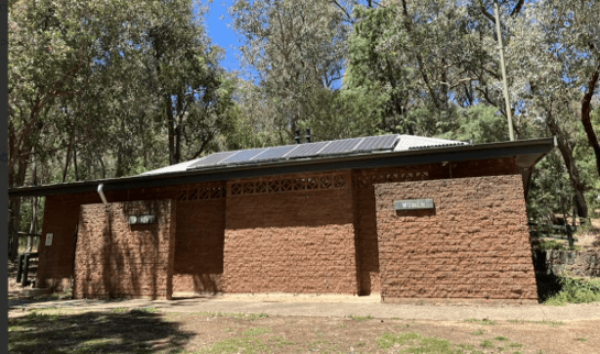 Brick toilet block in a bushland setting, with a metal roof fitted with solar panels and native trees surrounding the site.
