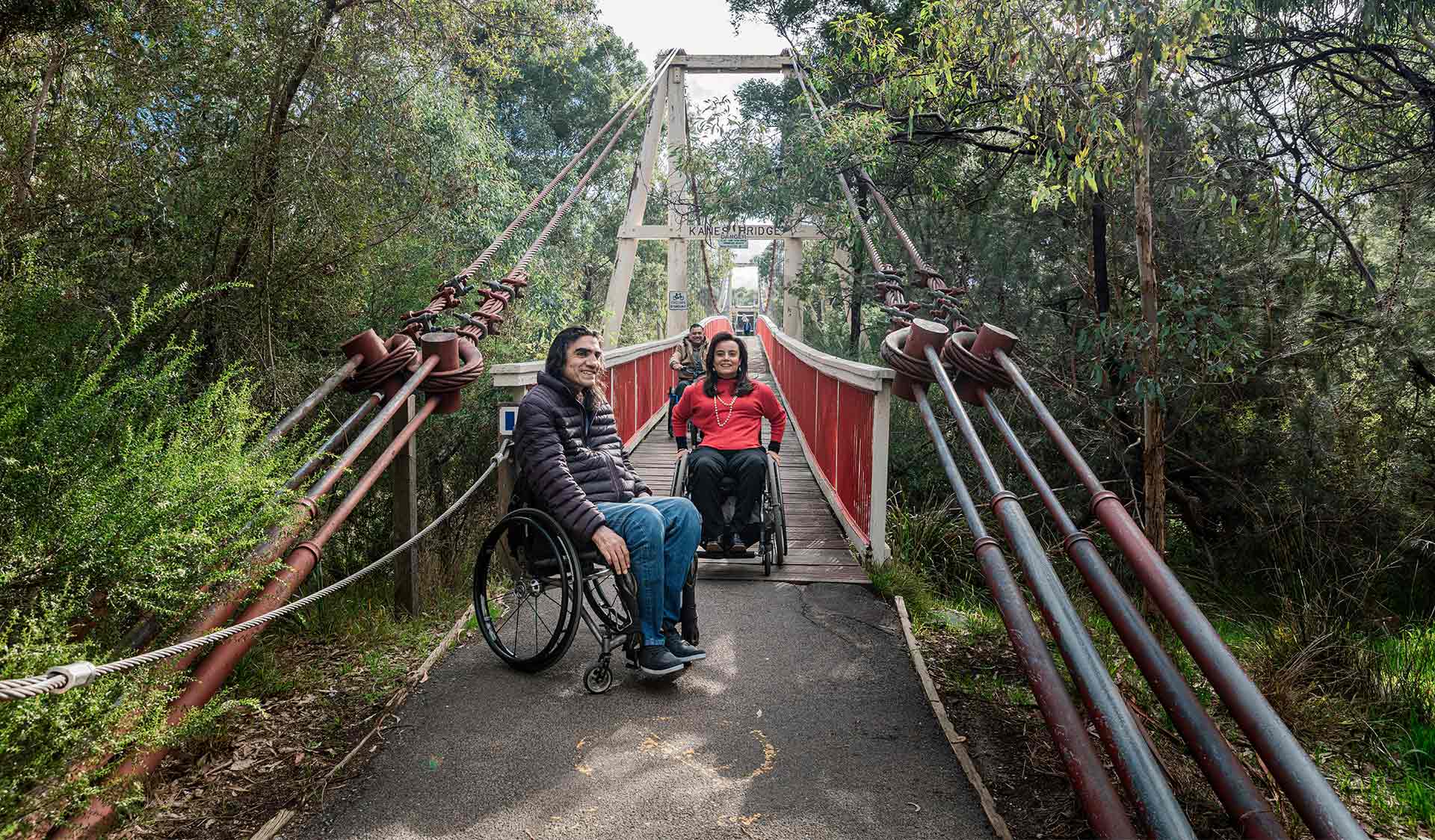 Man in wheelchair waits as his two friends cross accessible Kane's Bridge in Yarra Bend Park.
