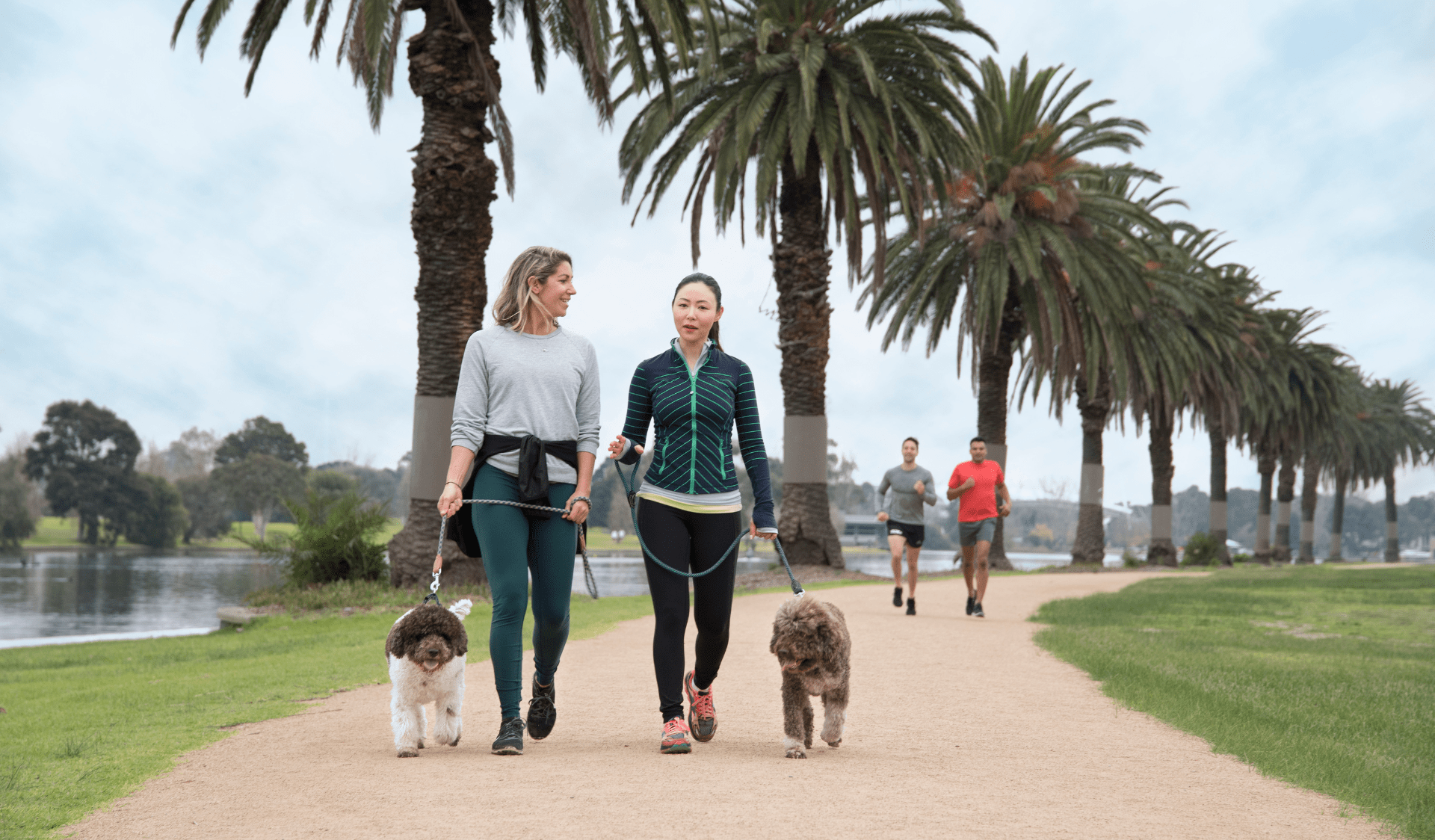 Two females walking their dogs on lead along gravel footpath next to the river