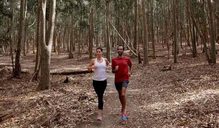 A couple run through the bush and leaves at Lysterfield Park.
