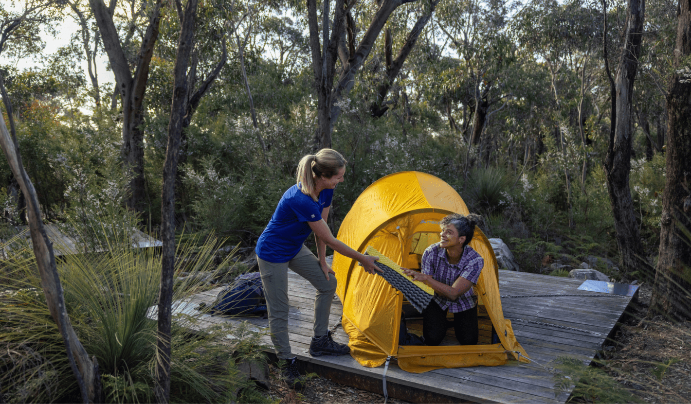 One person passing a mat to another person in their tent on a wood platform.